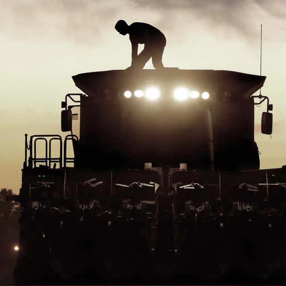 Silhouette of farmer on harvesting tractor at sunset Alberta